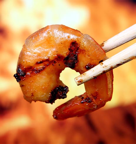 Gemarineerde scampi vastgehouden met chopsticks boven BBQ vuur